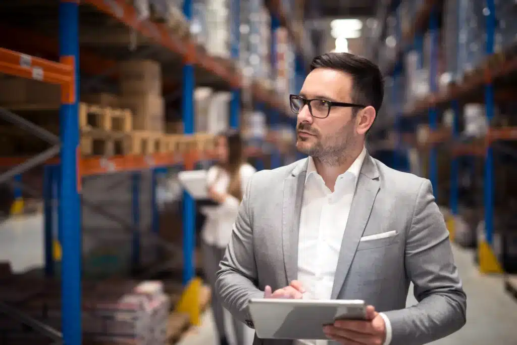 portrait successful businessman manager ceo holding tablet walking through warehouse storage area looking towards shelves 1